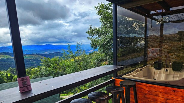 A balcony with a wooden railing, a hot tub, and two bar stools. - Hakuna Matata glamping (Monguí)