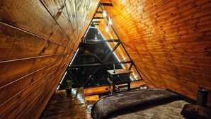 A narrow, wooden-paneled attic room with a sloped ceiling, a bed, and a small table. - Hakuna Matata glamping (Monguí)
