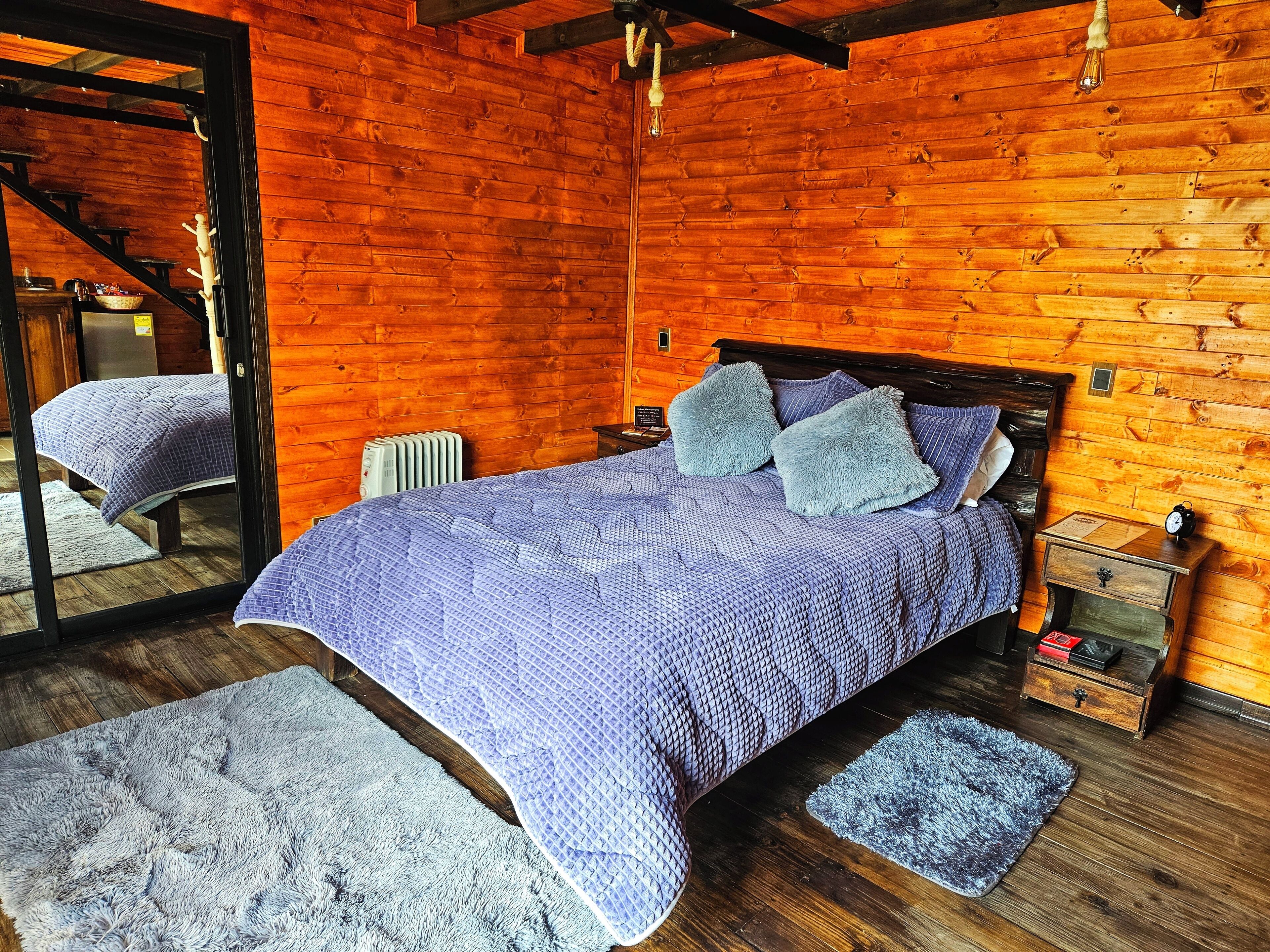 A cozy wooden cabin bedroom with a bed, pillows, a nightstand, and a mirror.