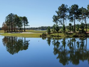 A serene golf course with a calm lake reflecting trees and a clear sky.