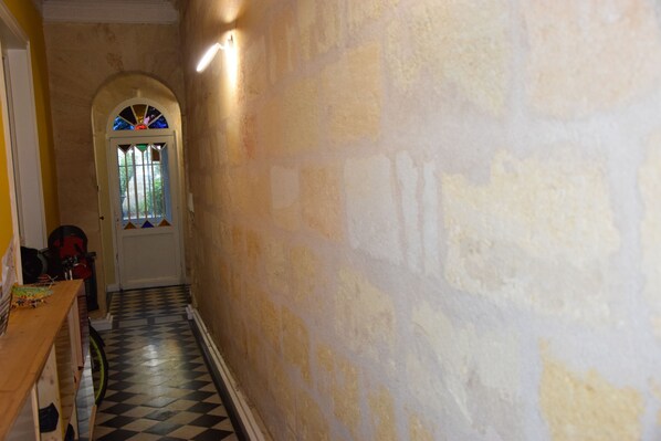 A narrow hallway with a checkered floor, a door with a stained glass window, and a wall with peeling paint.