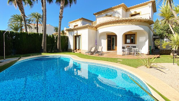 A poolside view of a two-story house with a swimming pool, outdoor seating, and palm trees. - Quiet and cozy villa near the beach (Denia)