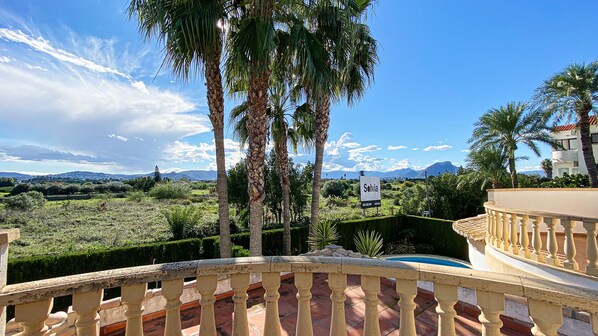 Varanda com vista para um jardim arborizado, palmeiras e montanhas ao longe.