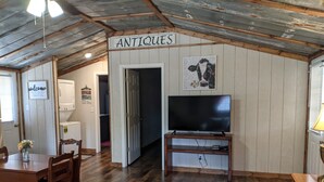 A rustic interior with a wooden ceiling, a TV on a wooden stand, a dining table with chairs, and a sign reading "ANTIQUES". - Private cabin located on 7 acres in the country (Columbia)