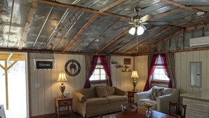 A cozy cabin interior with a wooden ceiling, a ceiling fan, a sofa, a dining table with chairs, and a fireplace. - Private cabin located on 7 acres in the country (Columbia)