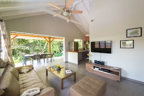 A spacious living area with a sofa, coffee table, and ottoman, a kitchen area, and a dining space with a view of the outdoors.