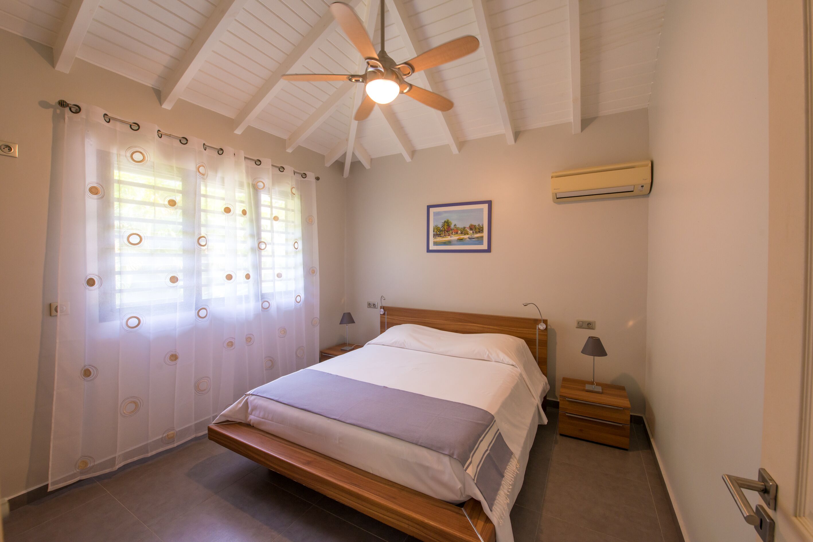 A bedroom with a wooden bed, a ceiling fan, a nightstand, a lamp, and a picture on the wall.