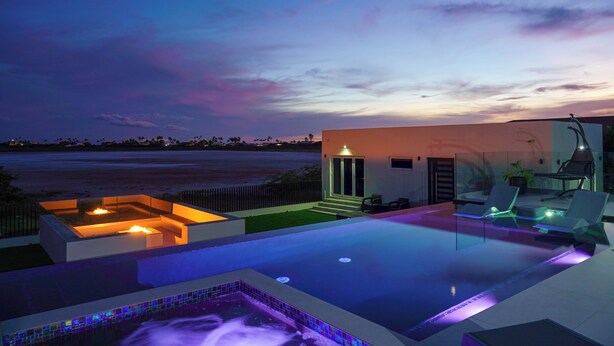 Un área de piscina moderna al aire libre con un jacuzzi, sillones de descanso y vista a la playa al atardecer.
