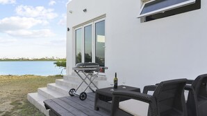 Un patio con una parrilla, una mesa y sillas al aire libre, con vista a un cuerpo de agua.