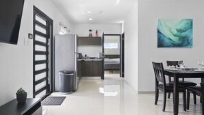 Una cocina moderna con refrigerador, pileta y encimera. Hay un comedor con mesa y sillas, y un cuadro en la pared.