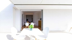 Een moderne eethoek met een witte tafel en stoelen, een potplant en uitzicht op de aangrenzende kamer.