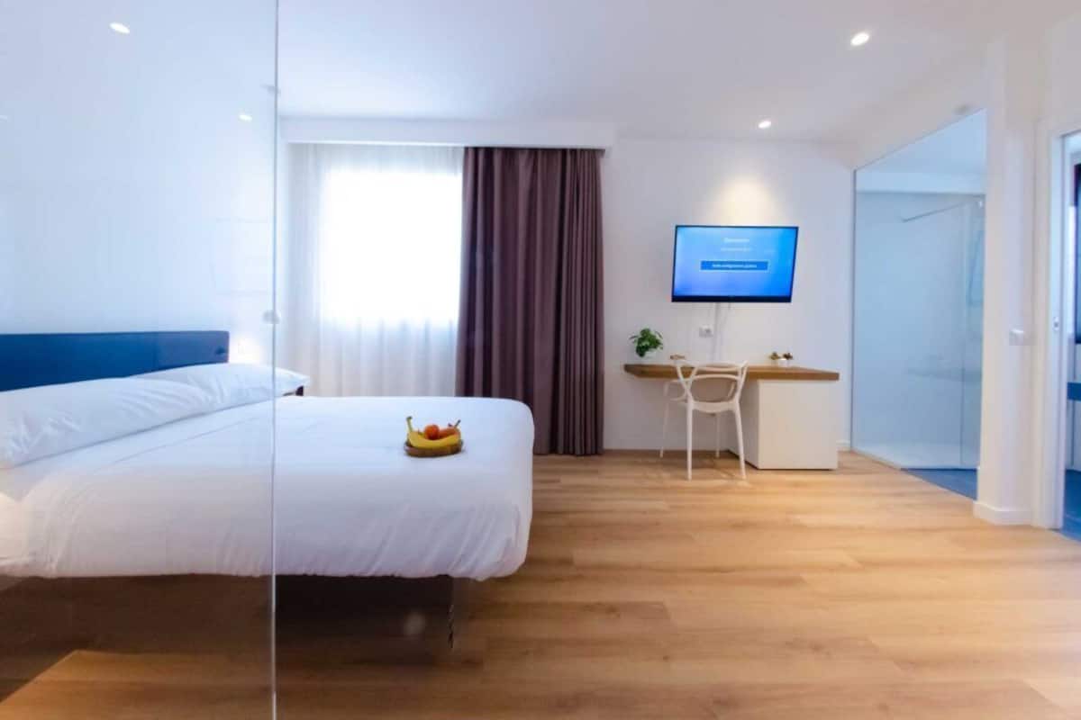 Ein modernes Hotelzimmer mit Bett, Schreibtisch, Computer und Fernseher.