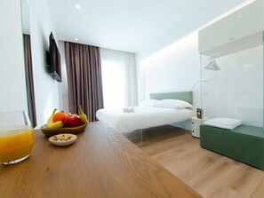 A hotel room with a bed, a bedside table with fruits and a glass of orange juice, a green sofa, and a glass shower enclosure. - Pascià boutique hotel (Ragalna)