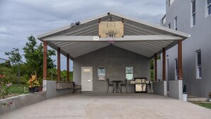Ein überdachter Patio-Bereich mit Basketballkorb, Gartenmöbeln und Grill.