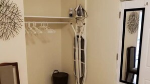 Ein Zimmer mit einem Stuhl, einem Kleiderhaken, einem Mülleimer und einer Tür mit Spiegel.