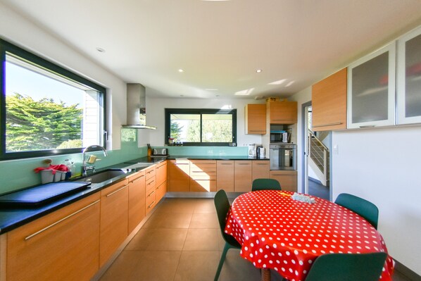 A modern kitchen with a dining area, large windows, and a view of greenery. - Recently refurbished villa with sea views, closed garden and 80 m from beach. (Tregunc)