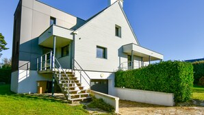 A modern two-story house with a staircase leading to a balcony, surrounded by a well-maintained lawn and a hedge. - Recently refurbished villa with sea views, closed garden and 80 m from beach. (Tregunc)