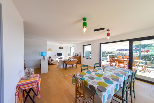 A spacious living area with a dining table, chairs, a TV, and a balcony with outdoor seating. - Recently refurbished villa with sea views, closed garden and 80 m from beach. (Tregunc)