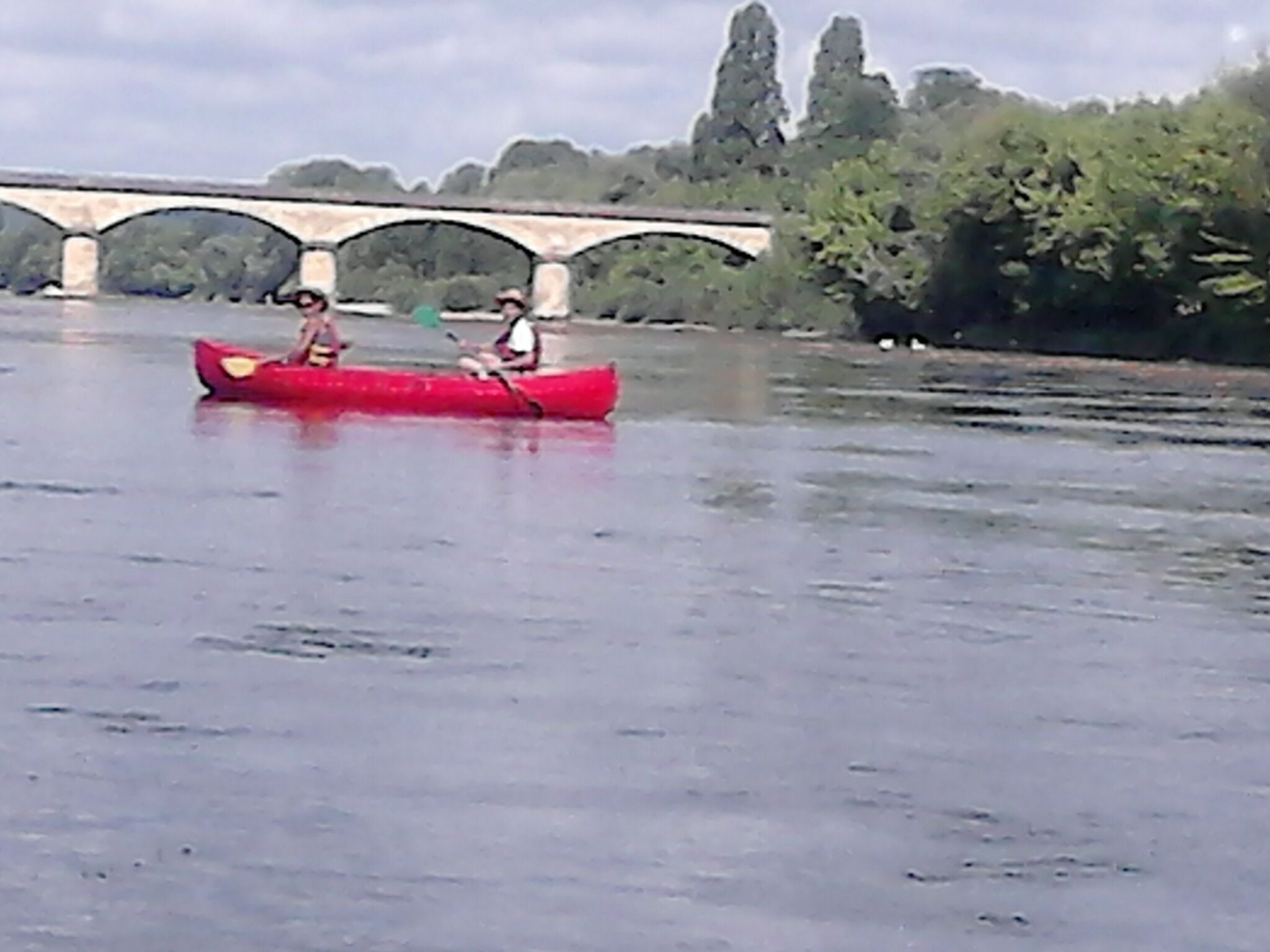 A red canoe on a river with a bridge in the background.