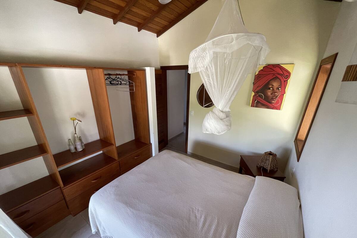 A bedroom with a bed, wooden wardrobe, and a hanging mosquito net.