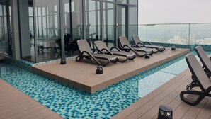 Un área de piscina en la azotea con sillones de descanso y un espacio cubierto de cristal.