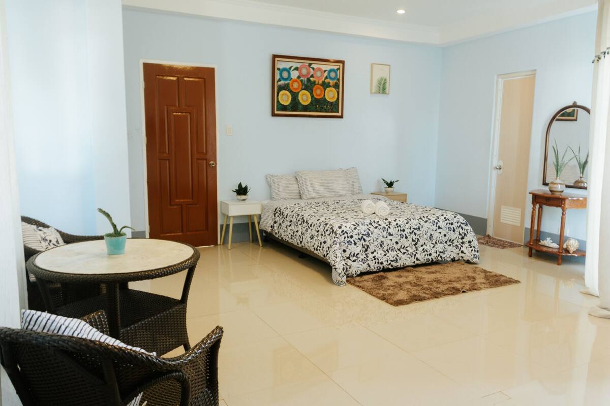 A bedroom with a bed, a small table, a chair, and a door.