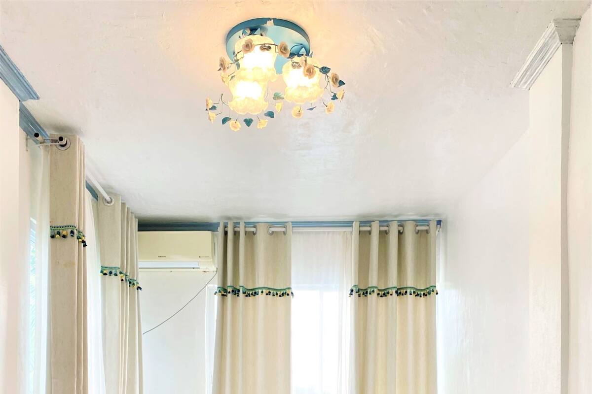 A bedroom with a bed, curtains, a chandelier, and a nightstand with a lamp.