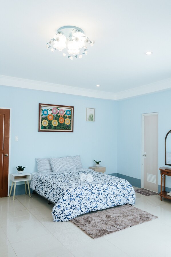 A bedroom with a bed, a nightstand, a small table, a chair, a door, and a ceiling light fixture.