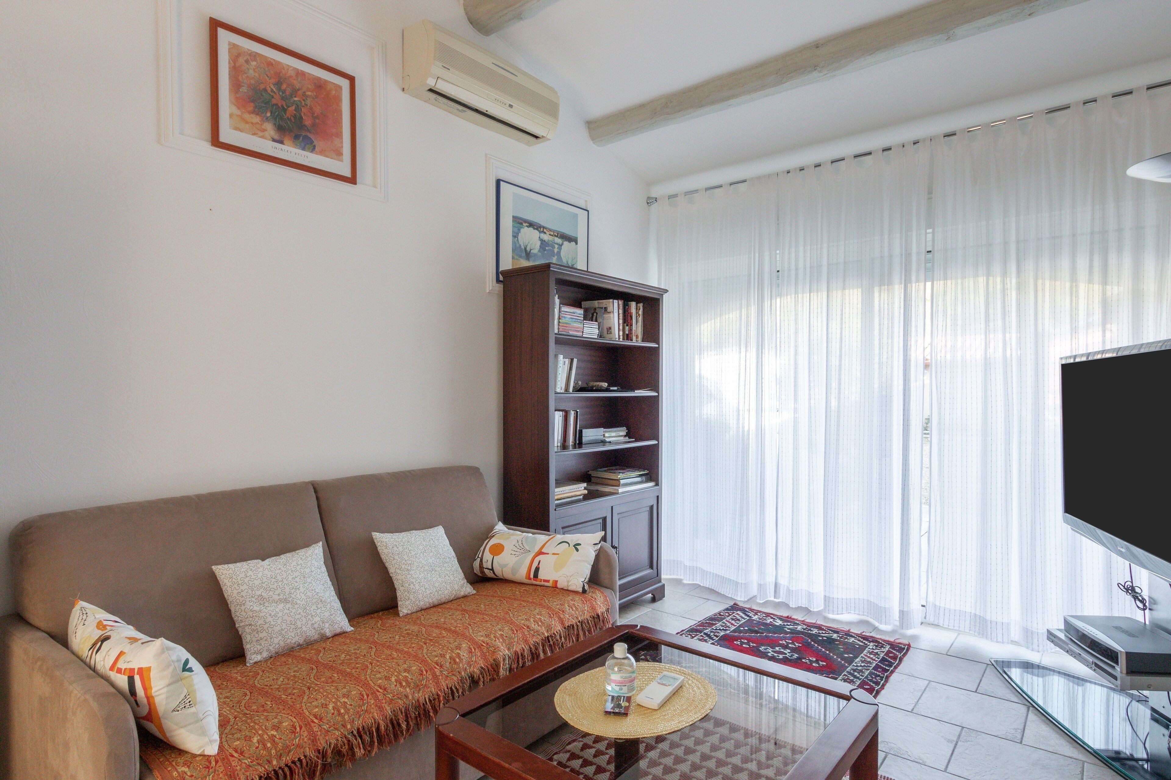 A living room with a brown sofa, a wooden bookshelf, a glass coffee table, and a flat-screen TV.