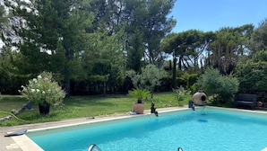 Una piscina amb aigua blava i cristal·lina, envoltada d'una zona enjardinada amb arbres i plantes en testos.