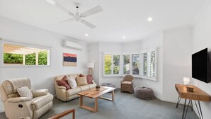 Un salon spacieux doté d’un ventilateur de plafond, d’un canapé, d’une table basse, d’un téléviseur et de grandes fenêtres.
