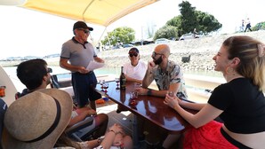 Un grupo de personas sentadas en una mesa en un barco, con una costa rocosa y árboles al fondo.