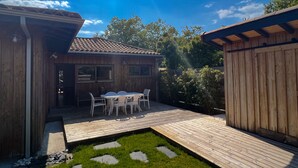 Ein Holzhaus mit Terrasse, einem Tisch mit Stühlen und einem kleinen Garten.