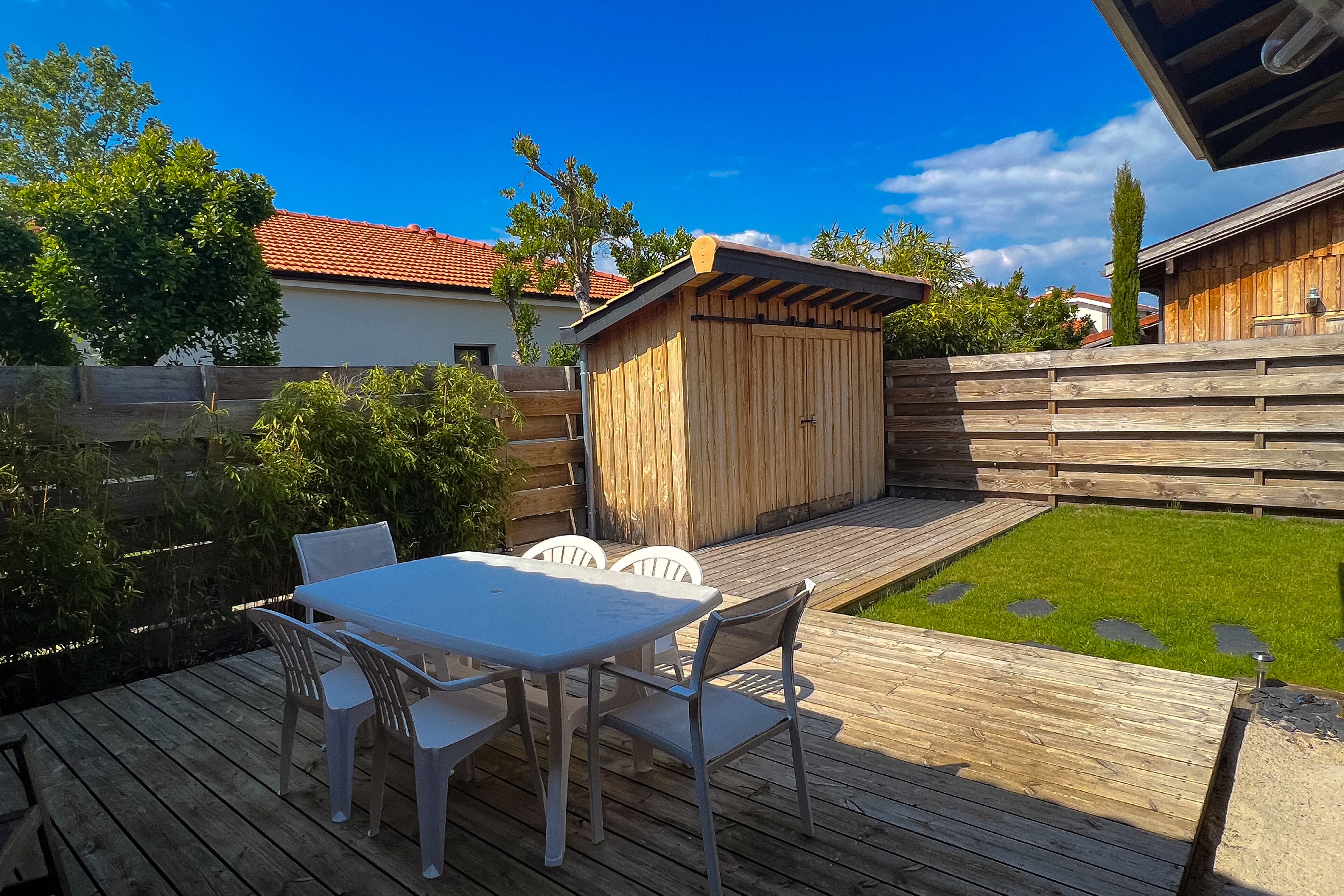Une terrasse en bois avec une table et des chaises, un petit abri de jardin et une pelouse bien entretenue.