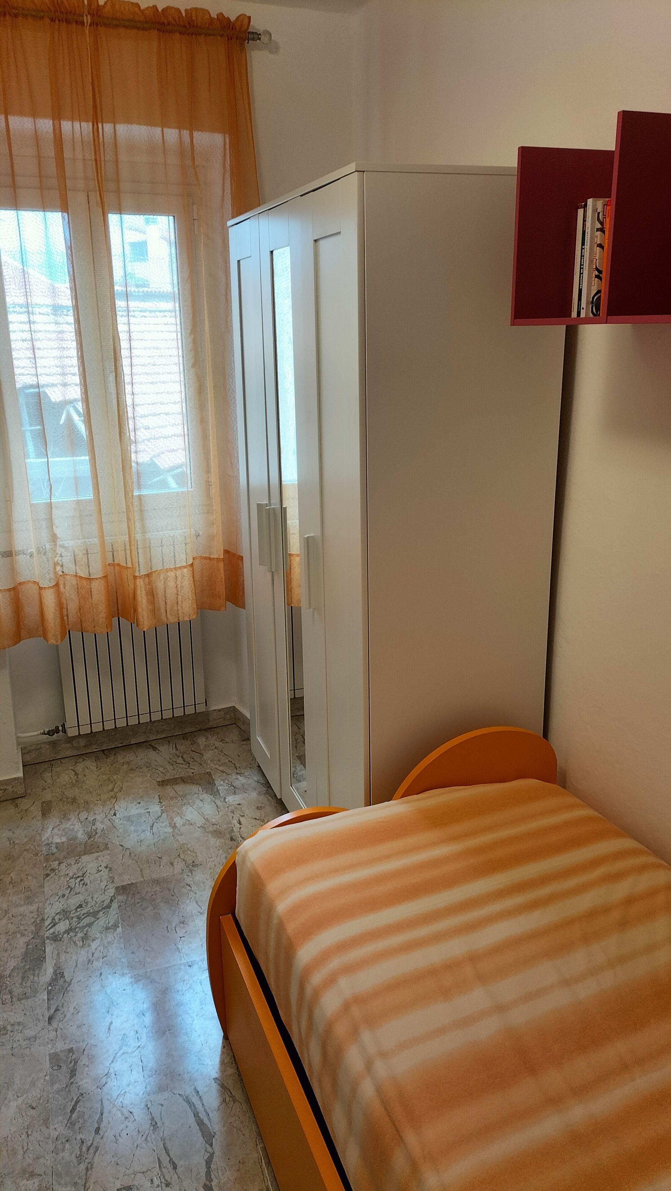 A bedroom with a bed, a wardrobe, a radiator, and a window with curtains.