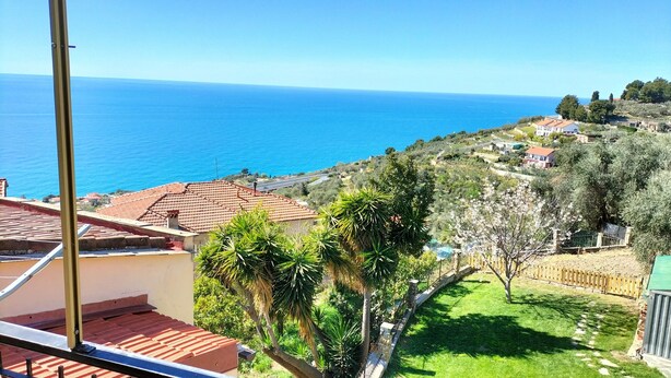 Vista costera con mar azul cristalino, edificios con tejados de terracota y vegetación exuberante.