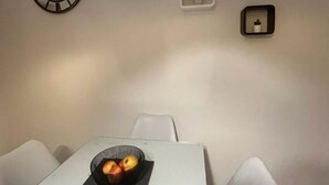 Una habitación con una mesa blanca, dos sillas, un reloj de pared y tres objetos pequeños enmarcados.