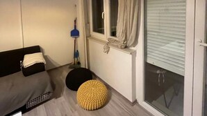 Una habitación con un sofá de color oscuro, un banquillo amarillo, una ventana con cortinas y un ventanal corredizo.