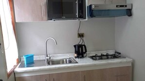 Una cocina compacta con microondas integrado, estufa a gas, pileta y alacenas de madera.