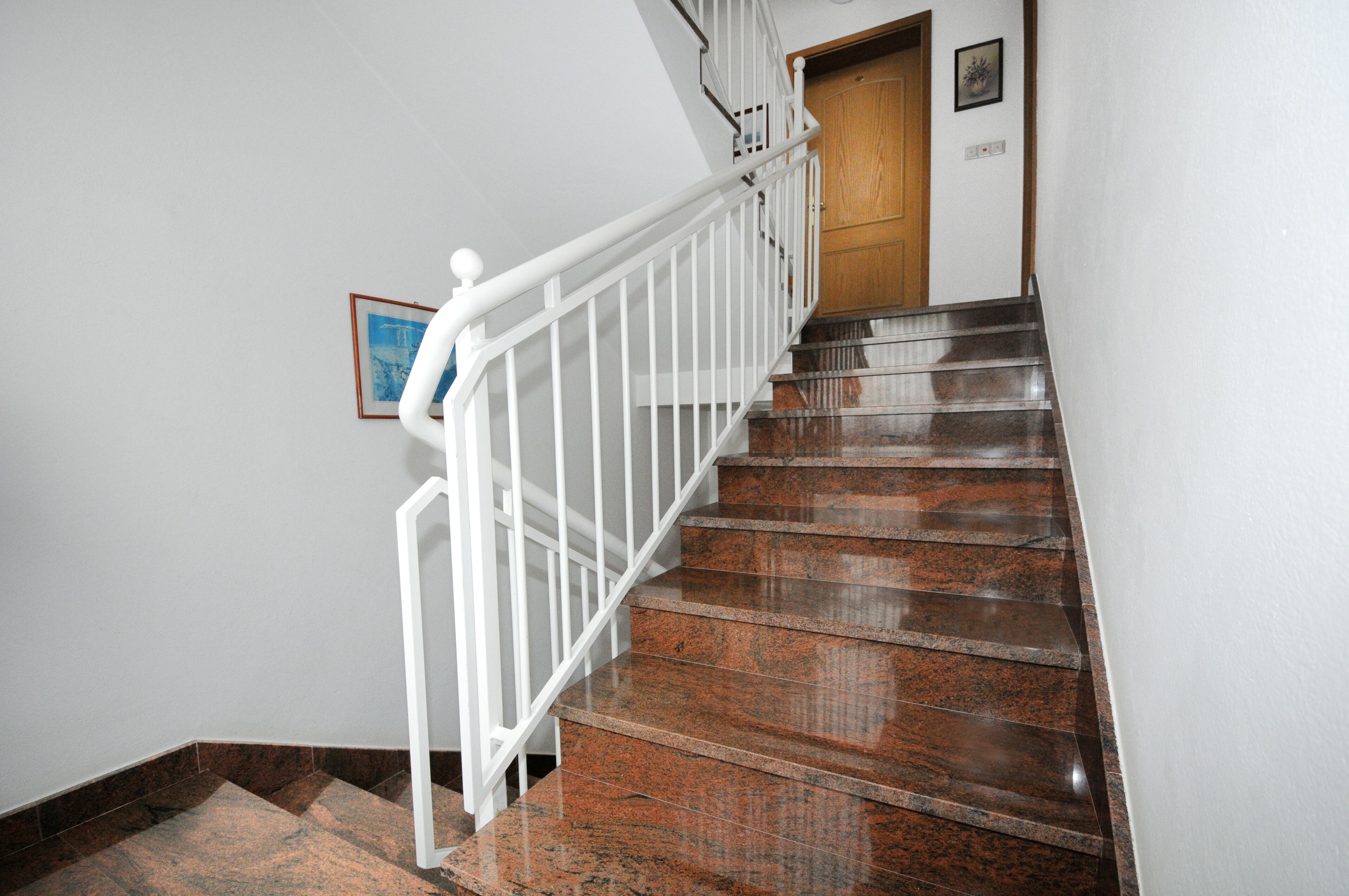 Un escalier avec une rampe blanche, une porte en bois et un tableau encadré accroché au mur.