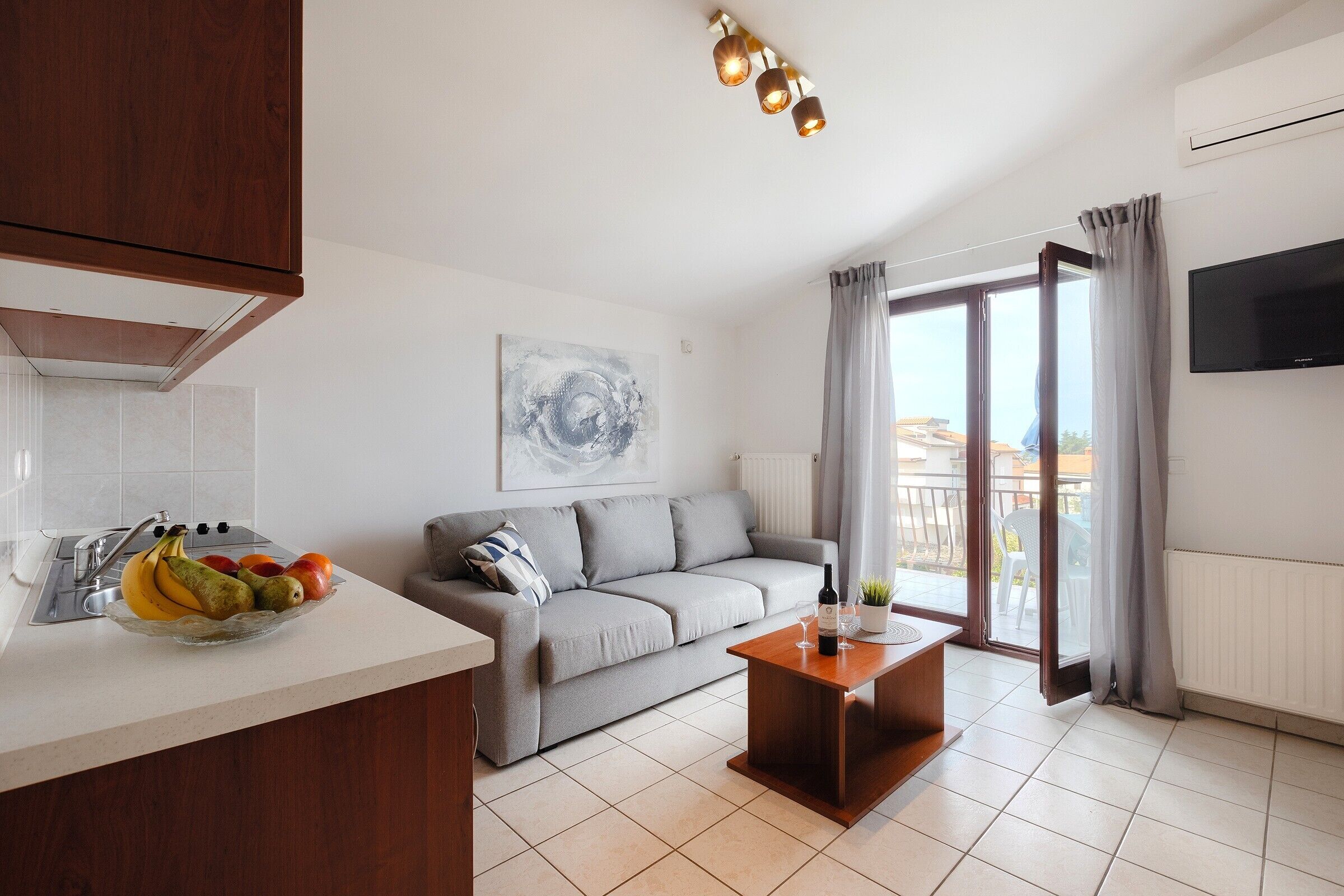 A modern living room with a sofa, a coffee table, a TV, and a balcony with curtains.