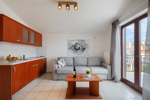Une cuisine moderne avec des meubles en bois, une table à manger avec une bouteille et un verre, et un canapé gris surmonté d’un tableau.