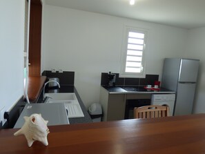 Uma cozinha compacta com pia, torradeira, cafeteira, geladeira e uma janela.