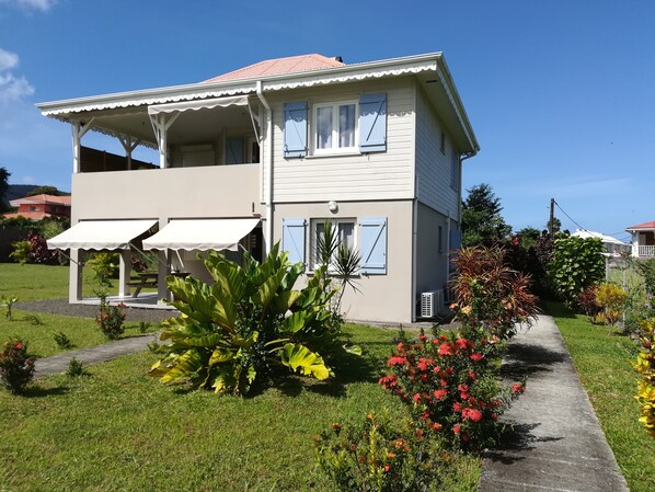 A two-story house with a balcony, a covered porch, and a garden with various plants and flowers. - Les Deux Mers: A one-story residence with an additional floor, 150 m from the beach. (Les Trois Ilets)
