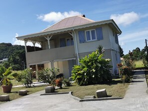 A two-story house with a balcony, surrounded by a garden with potted plants and a lawn. - Les Deux Mers: A one-story residence with an additional floor, 150 m from the beach. (Les Trois Ilets)