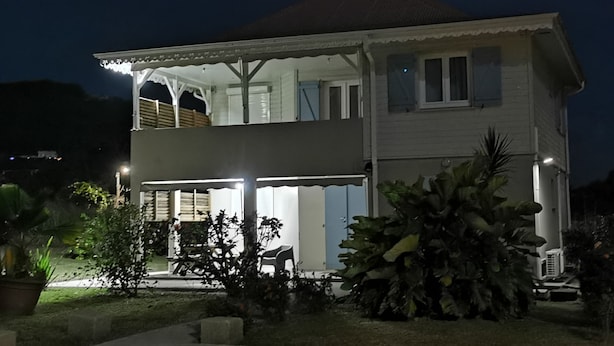 Une maison à deux étages avec un balcon, une véranda et un grand arbre dans le jardin.