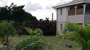 Un bâtiment à l’extérieur blanc et au toit rouge, entouré d’une pelouse bien entretenue et de diverses plantes tropicales.