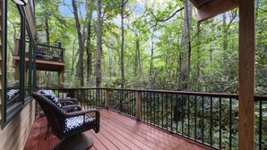 A wooden deck with wicker chairs and a view of a forest.