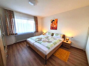Une chambre à coucher avec un lit, des lampes de chevet, un radiateur, une fenêtre avec des rideaux et un tableau au mur.