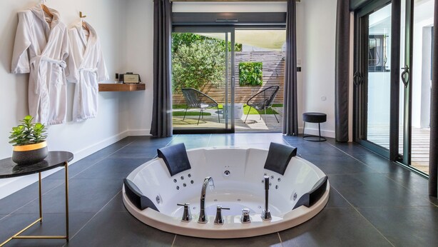 A modern bathroom with a large bathtub, a small table with a plant, and a seating area with a chair and a bench.